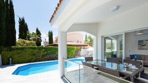 Un área de estar moderna al aire libre con una mesa y sillas de vidrio, una piscina y vistas del paisaje circundante.