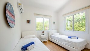 Una habitación con dos camas, una mesita, un reloj de pared y una ventana con vistas a zonas verdes.