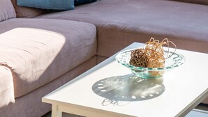 Una mesa blanca con un cuenco de vidrio y adornos, ubicada frente a un sofá rosa con almohadas azules y blancas.