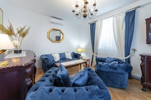 Un salon avec un canapé bleu, une table basse en bois, un lustre et un grand miroir au mur.