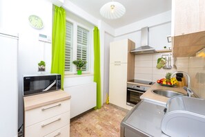 Une cuisine compacte équipée d’un four à micro-ondes, d’une cuisinière, d’un évier et d’une petite fenêtre avec des rideaux.