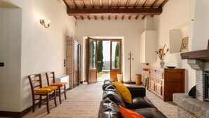 A spacious living room with a leather sofa, wooden chairs, a fireplace, and a view through a glass door. - Casale Santa Francesca - Country Villa with swimming pool in Orcia Valley, Tuscany (Campiglia D'orcia)