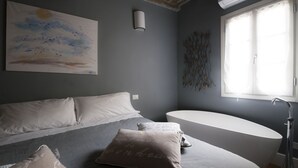 Een slaapkamer met een bed, een badkuip, een schilderij en een raam.