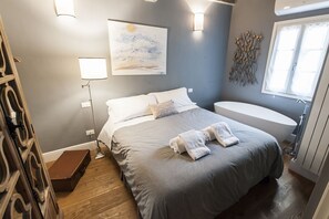A bedroom with a bed, bedside lamps, a painting, a window, and a bathtub. - Little and cozy apartment in the San Lorenzo district, full of restaurants and shops. (Firenze)
