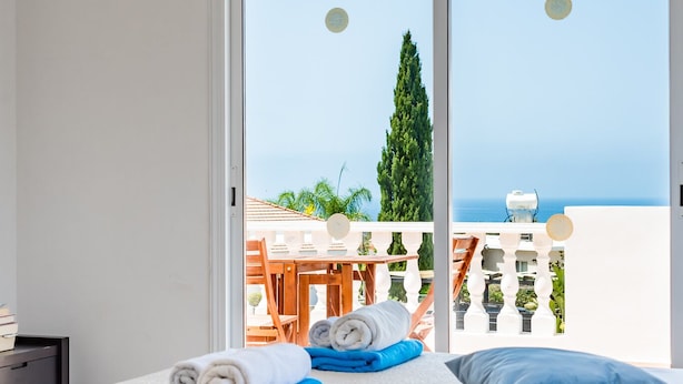 A bedroom with a bed, a view of the sea, and a balcony with a table and chairs. - Villa Alysia by Ezoria Villas (Paphos)