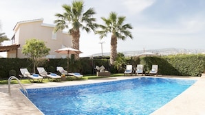 A swimming pool with lounge chairs and umbrellas, surrounded by palm trees and a view of the city. - Villa Alysia by Ezoria Villas (Paphos)