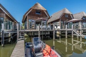 Una casa de madera con techo de paja, un muelle y un bote con chalecos salvavidas.