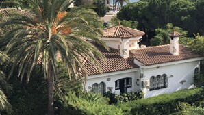 Een landhuis aan de kust met een pannendak, omringd door weelderige begroeiing en uitzicht op zee.
