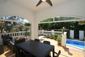 Une terrasse couverte avec une piscine, des meubles d’extérieur et des plantes en pot.