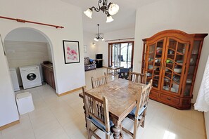 A dining area with a wooden table and chairs, a chandelier, a washing machine, and a cabinet with glass doors.
