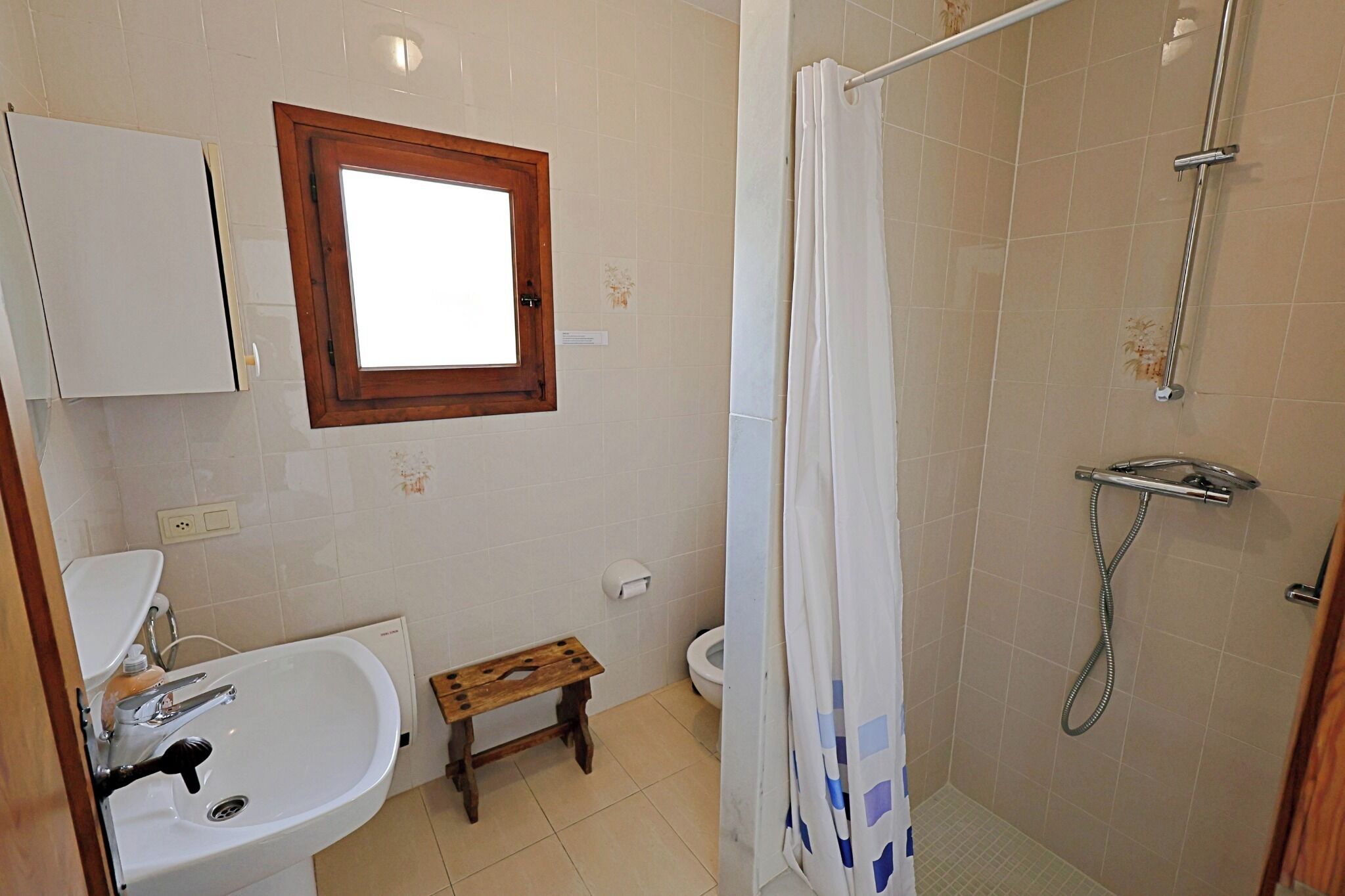 Un baño con lavamanos, inodoro, ducha y un taburete de madera.