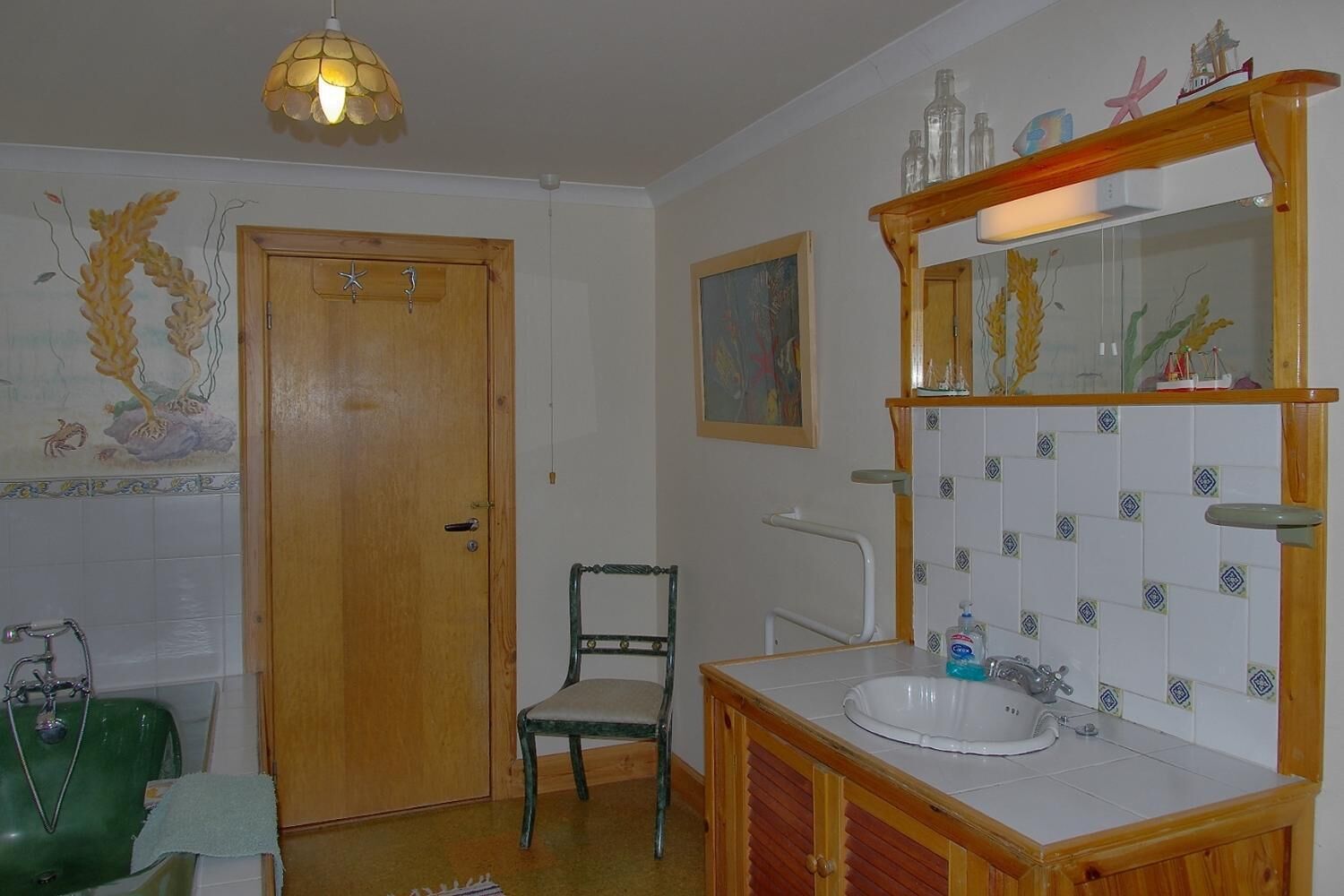 Un bany amb una porta de fusta, una cadira verda, un lavabo amb mirall i rajoles decoratives.