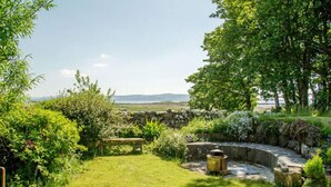 Un jardin avec un banc en pierre, une structure circulaire en pierre et une vue sur des collines lointaines.