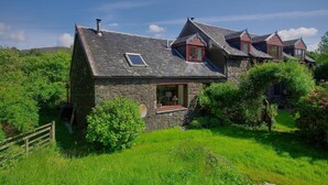 Une maison en pierre avec un toit en pente, une petite fenêtre et un jardin.