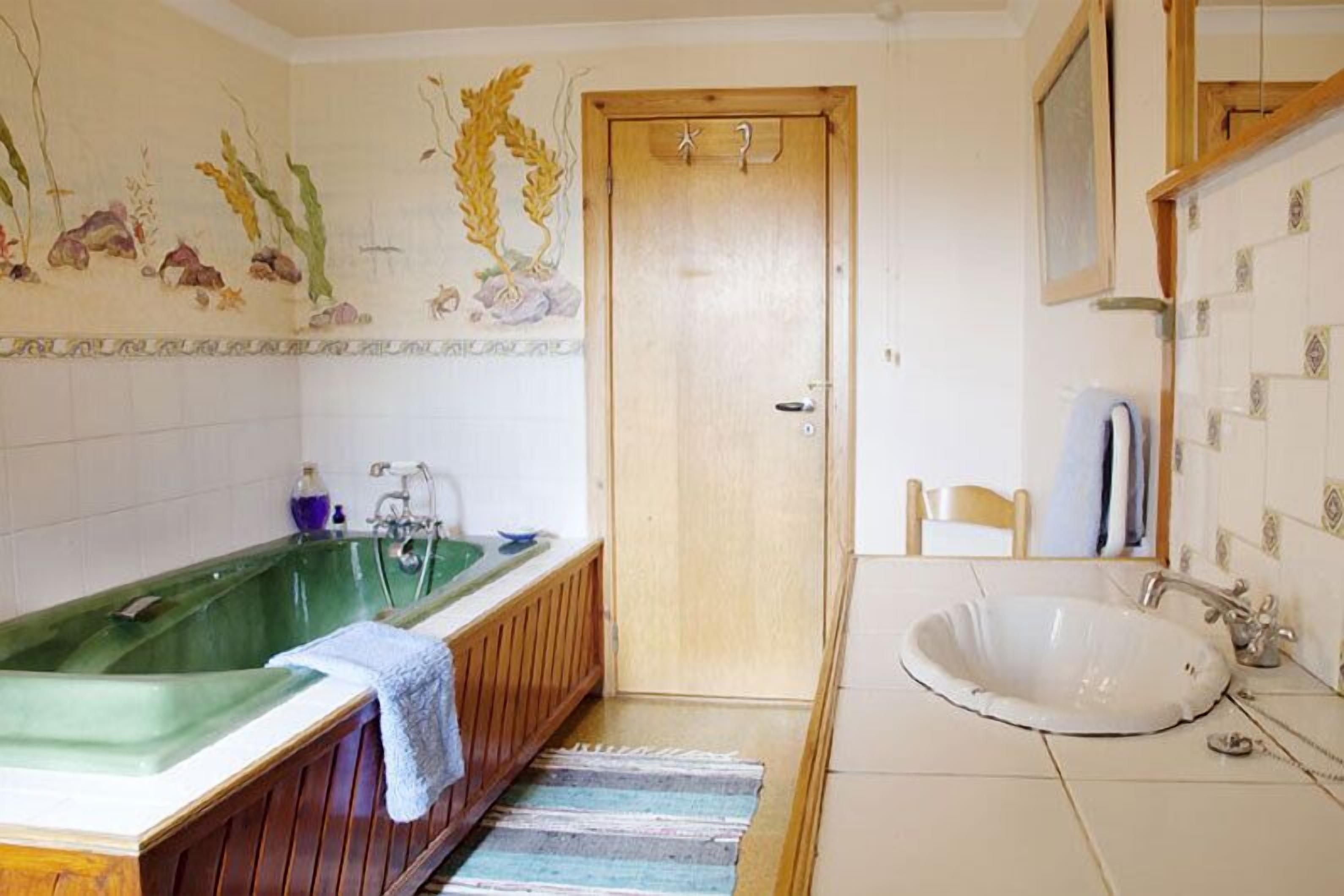 Uma casa de banho com uma banheira de hidromassagem verde, uma pia branca e uma porta de madeira.