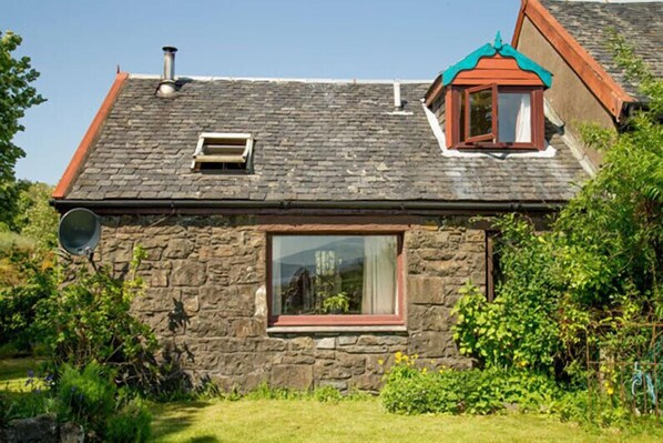 A stone house with a sloped roof, a small dormer window, and a satellite dish. - Steading Holidays - The Byre (Acharacle)
