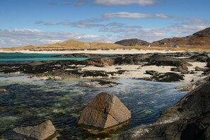 A rocky beach with clear water, sandy areas, and distant hills. - Steading Holidays - The Byre (Acharacle)
