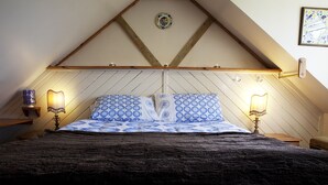 Une chambre avec un plafond en pente, un lit avec une literie à motifs, deux lampes de chevet et une assiette décorative accrochée au mur.