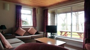 A cozy living room with a sofa, a coffee table, and a television. There is a window with curtains and a view of the outdoors. - Cottage 5 -  a cottages  that sleeps 6 guests  in 0 bedrooms (Irvinestown)
