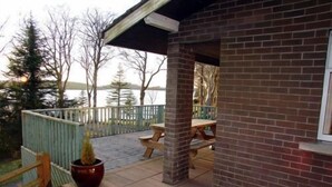 A brick building with a covered patio area, a wooden deck, and a view of a lake. - Cottage 5 -  a cottages  that sleeps 6 guests  in 0 bedrooms (Irvinestown)