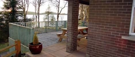 A brick building with a covered patio area, a wooden deck, and a view of a lake.