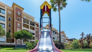 Ein Spielplatz mit einer Rutsche vor einem mehrstöckigen Gebäude mit Balkonen.