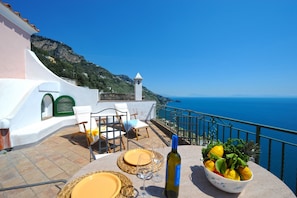 Eine Terrasse mit Tisch für zwei Personen, einer Weinflasche sowie Zitronen und Kräutern in einer Schale.