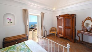 A bedroom with a balcony, a wooden wardrobe, a chair, and a bed with a green and white bedspread. - Casale Fralisa - Marvelous terrace and hot tub with sea view (Praiano)