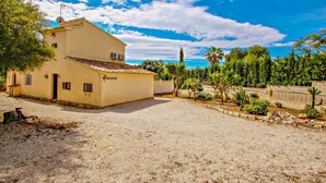 A two-story building with a beige facade, a gravel driveway, and a garden with various plants and a cactus. - Linea - sea view villa with private pool in Teulada (Teulada)