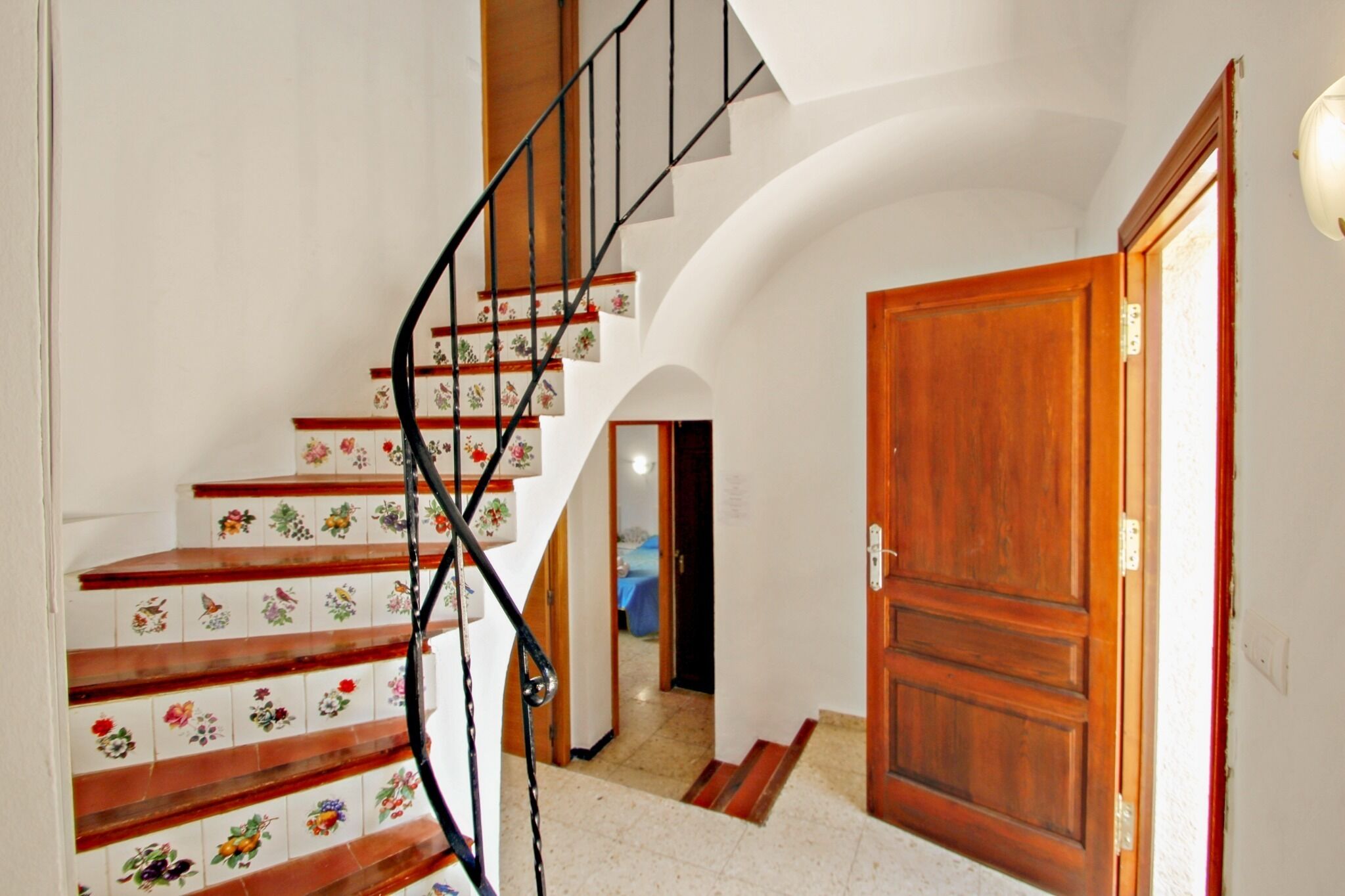 A staircase with floral tiles, a wooden door, and a spiral staircase.
