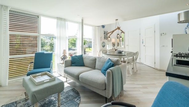 A spacious living area with a sofa, armchair, dining table, and kitchen area.