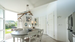 A modern kitchen with a dining area, white cabinetry, a built-in oven, and a large window overlooking a garden.