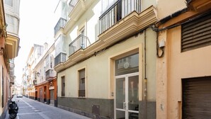 A narrow street lined with multi-story buildings, featuring balconies, large windows, and a closed shop with a glass door.