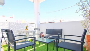 An outdoor patio with a table and chairs, surrounded by a white wall and a green lawn.