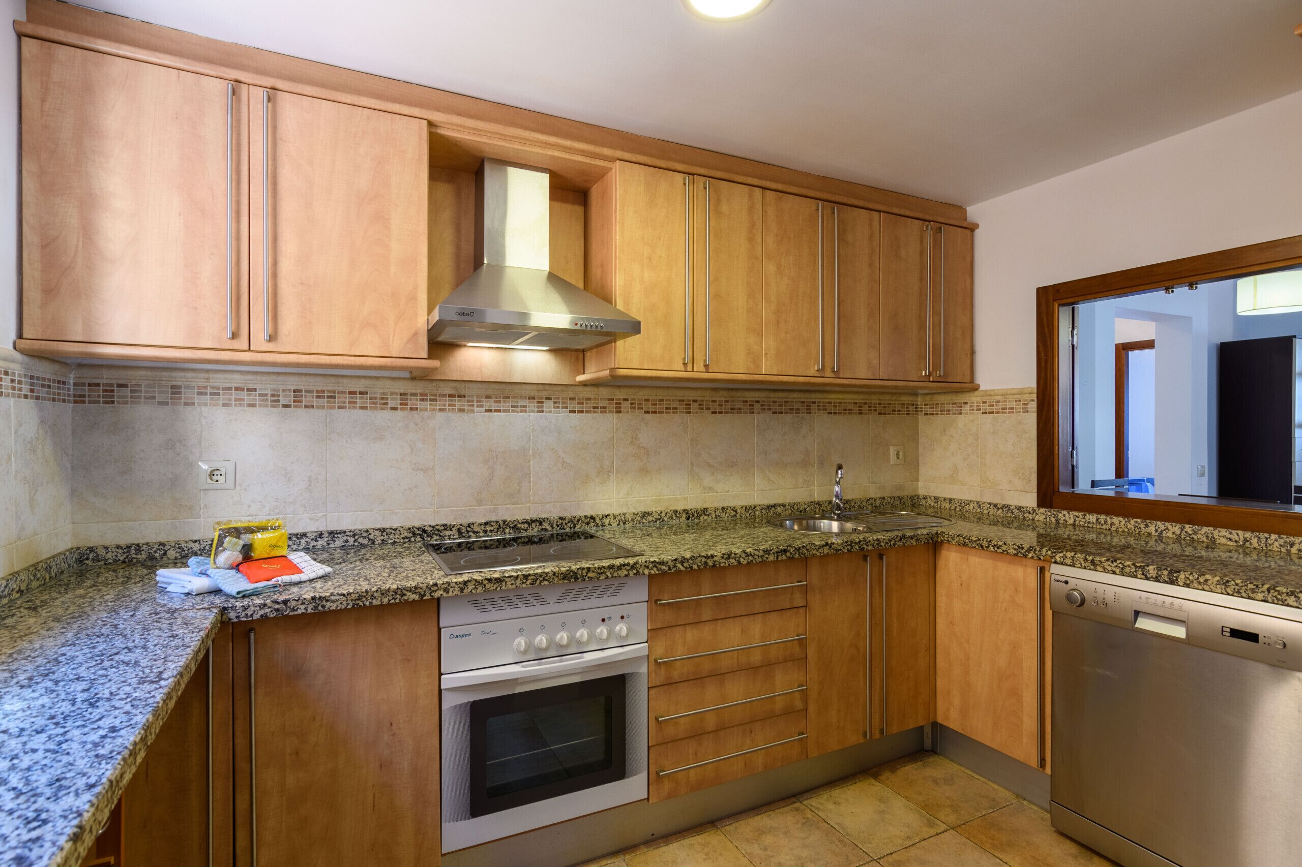 Una cocina con armarios de madera, campana extractora de acero inoxidable, horno empotrado, lavavajillas y encimera de granito.