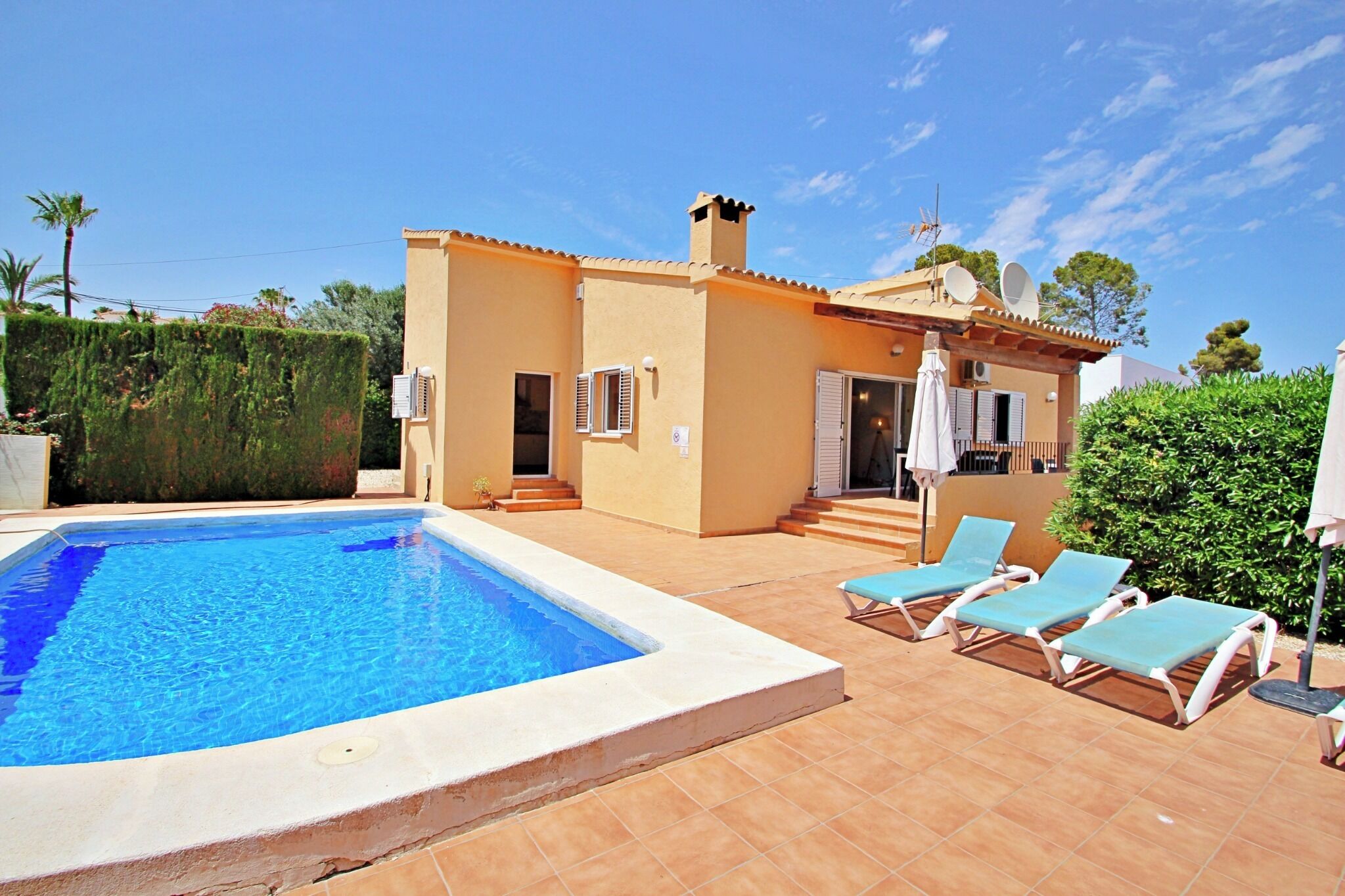 A poolside area with a swimming pool, a building with a tiled roof, and a few lounge chairs.