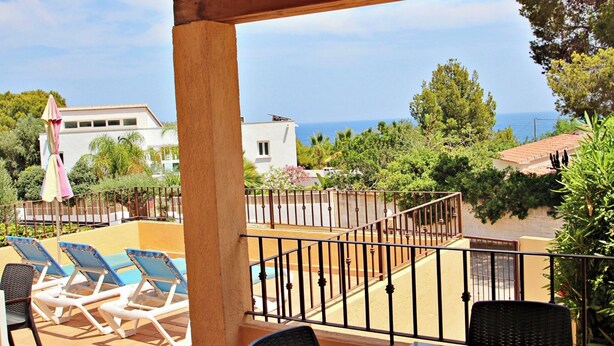 Un balcone con poltrone prendisole, una piscina e vista sul mare e sugli edifici circostanti.