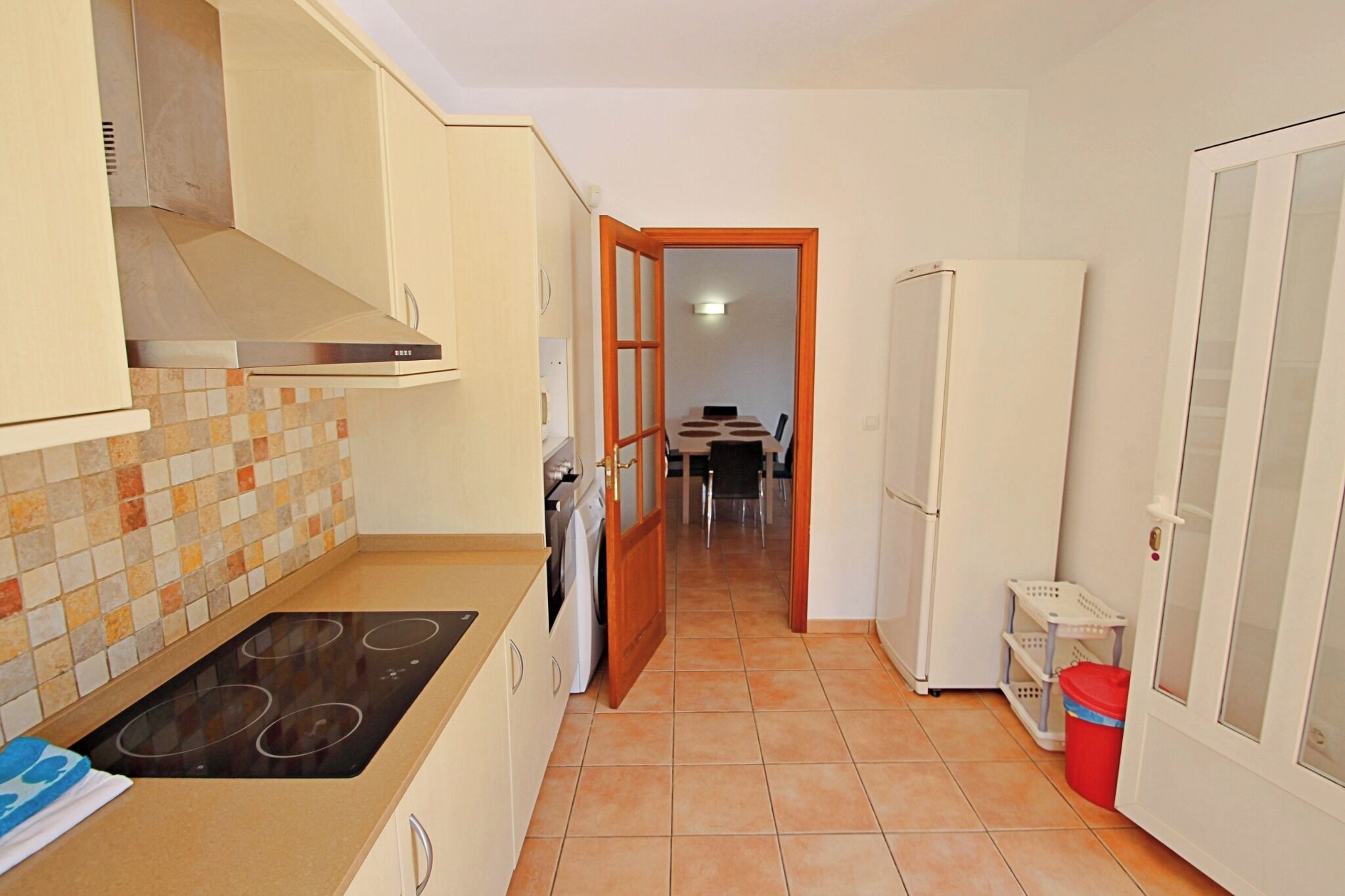 A kitchen with a stove, cabinets, and a tiled backsplash. There is a door leading to a dining area.