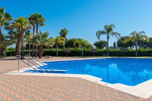 A swimming pool with palm trees, a brick deck, and a clear blue sky. - Prado Golf - Isla Canela Golf GPHG48P45 (Isla Canela)