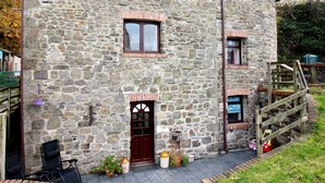 A stone building with a wooden staircase, a front door, and a small porch area with potted plants.
