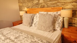 A bed with a wooden headboard, two nightstands with lamps, and a stone wall behind.