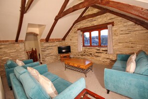 A cozy living room with stone walls, wooden beams, and blue sofas.