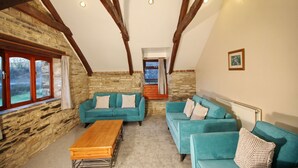 A cozy room with stone walls, wooden beams, and two teal sofas with patterned cushions. A wooden coffee table is in the center.