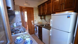 Una cocina compacta con armarios de madera, un refrigerador blanco, una lavadora y una estufa a gas.