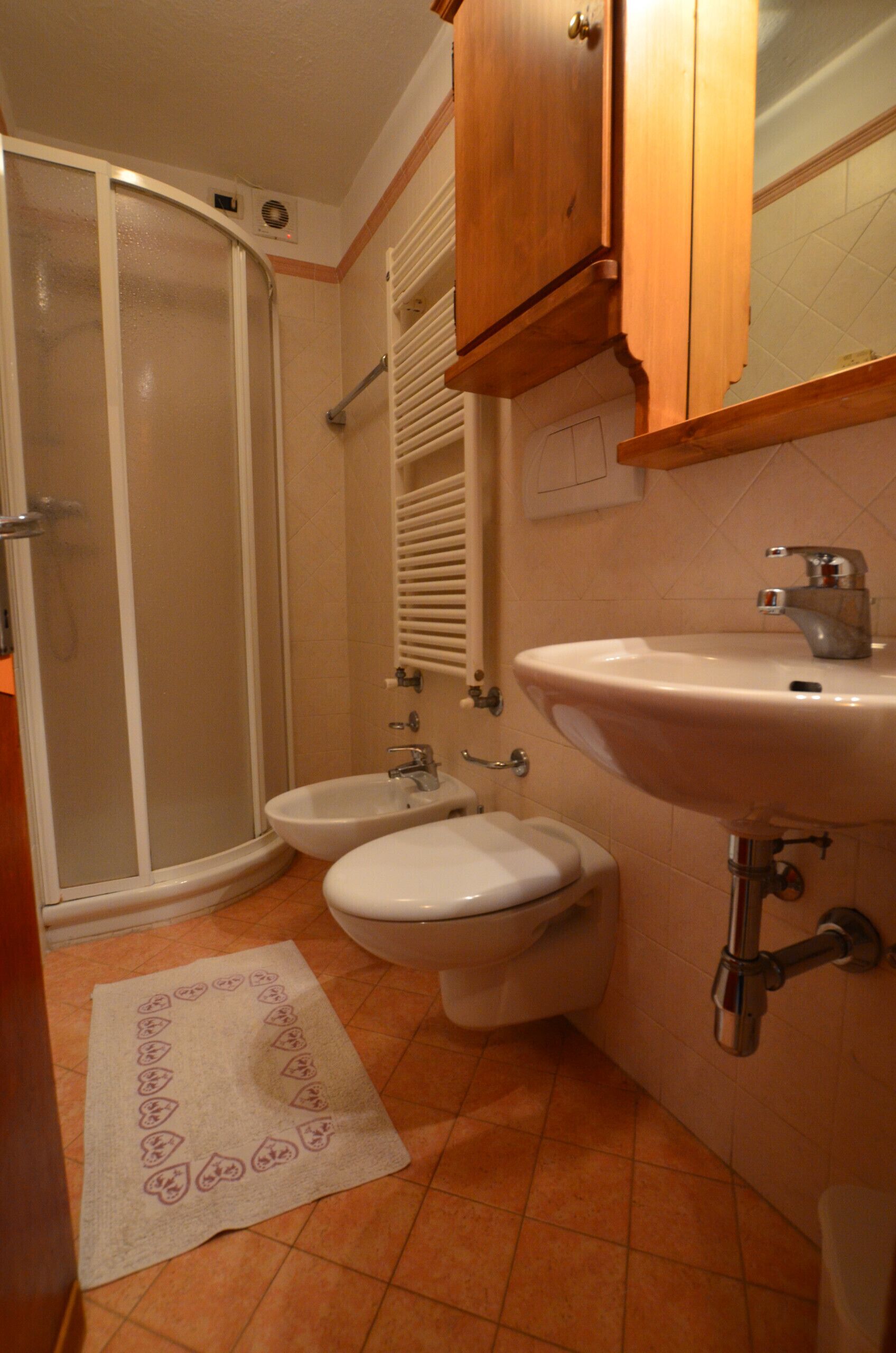 Een badkamer met een douche, toilet, bidet, wastafel en een houten kast.