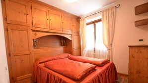 Una habitación con armarios de madera, una cama con ropa de cama roja y una ventana con cortinas.