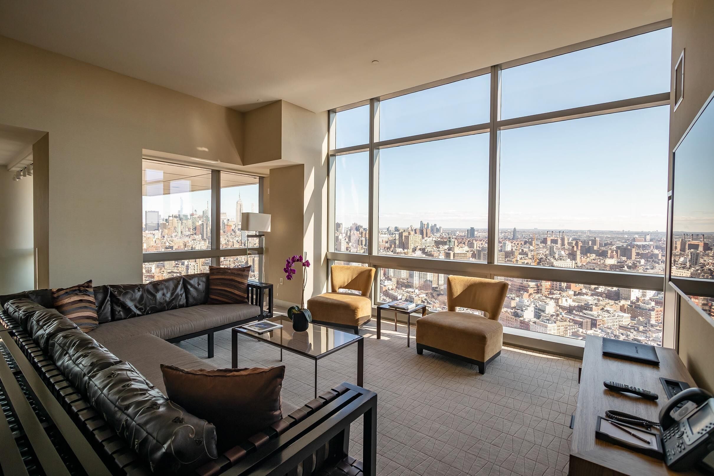 A spacious living room with a large city view, a leather sofa, two armchairs, and a coffee table.