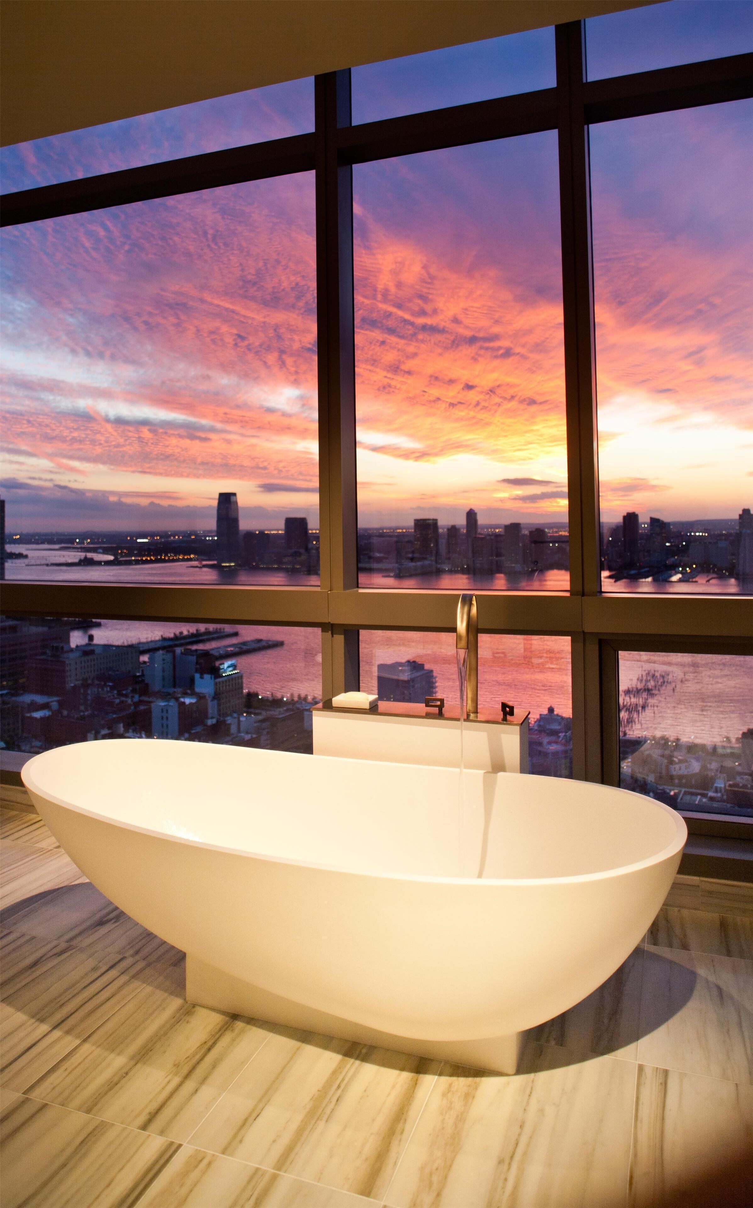 Une salle de bain moderne avec une baignoire sur pieds, un miroir et une fenêtre donnant sur le paysage urbain.