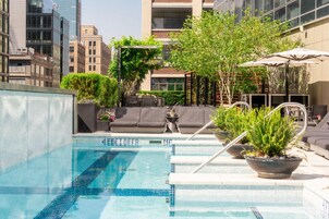 Una piscina en la azotea con una fuente de agua cristalina, rodeada de macetas con plantas y mobiliario de exterior.