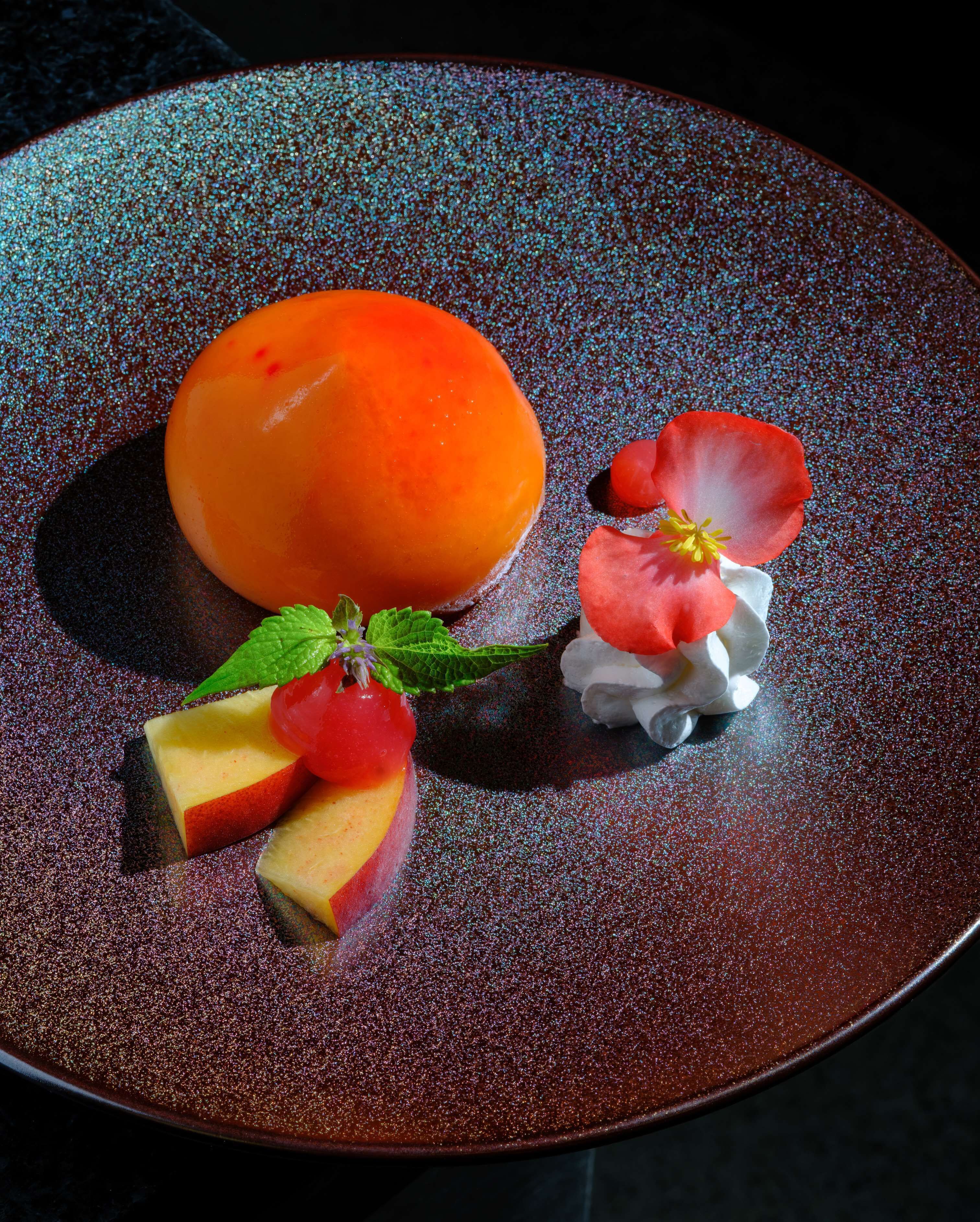 Un plato de postre con un melocotón, una fresa y una hoja de menta.